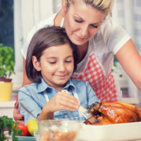 Young girl basting a chicken with her mother.